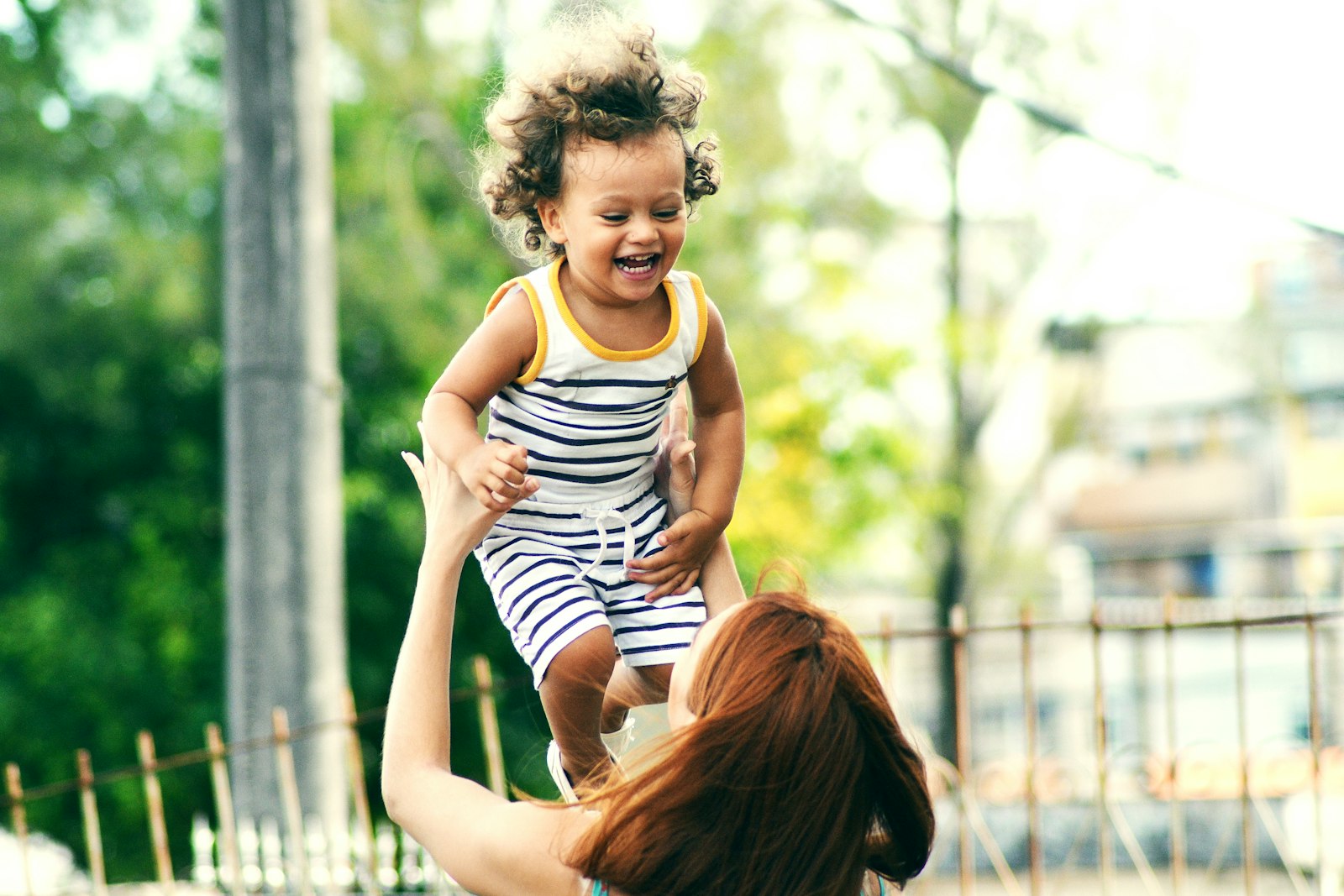 A caregiver lifting a laughing toddler into the air, mid-play
