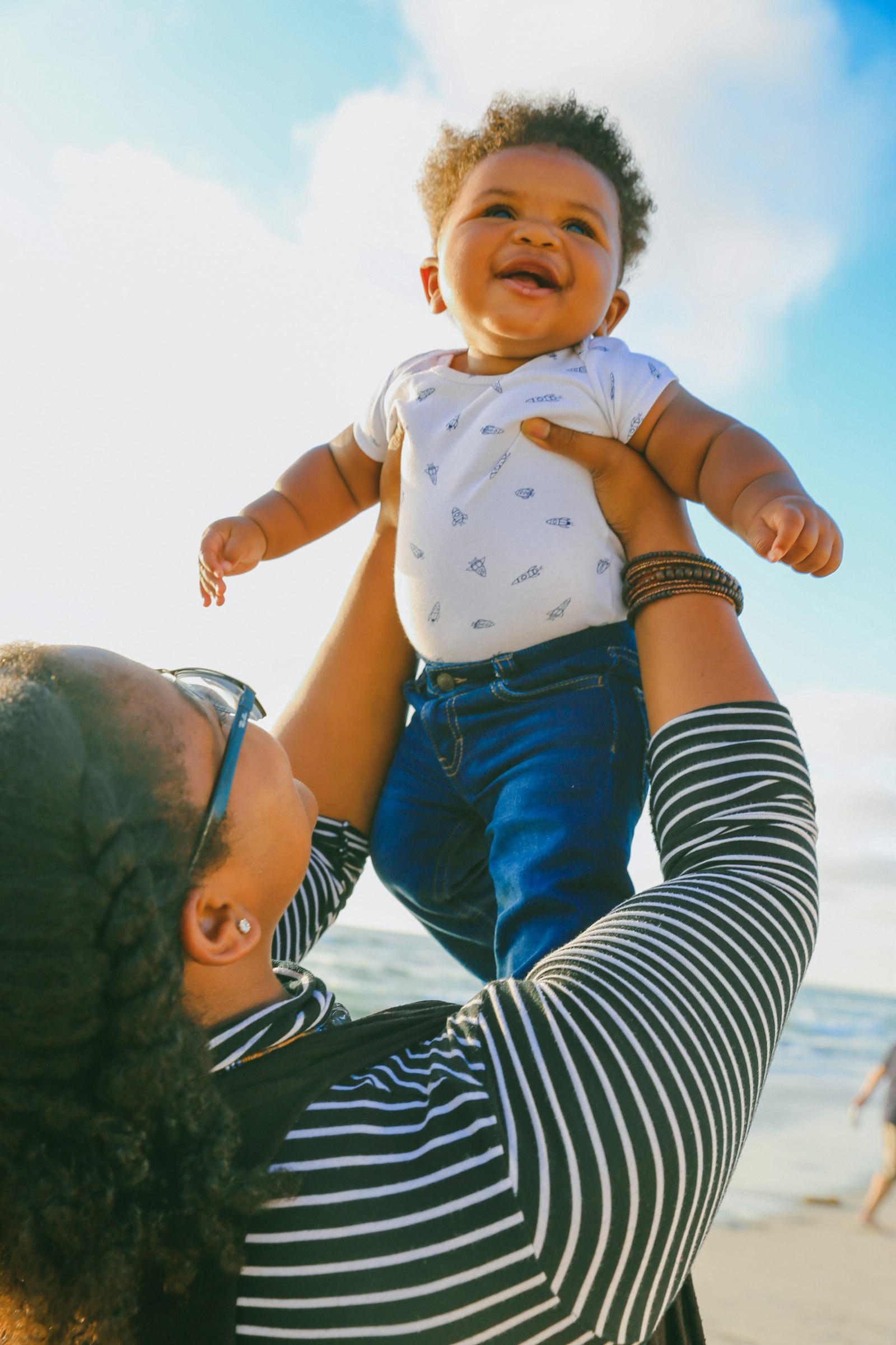 A parent joyfully lifting a smiling baby toward a bright sky