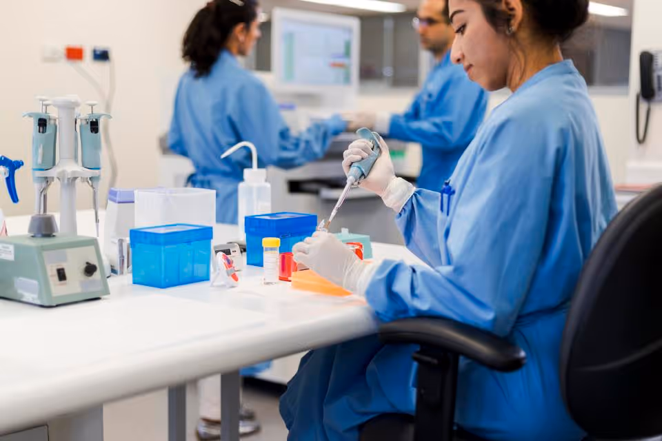 A researcher using a micropipette to prepare samples in a laboratory, with colleagues working in the background
