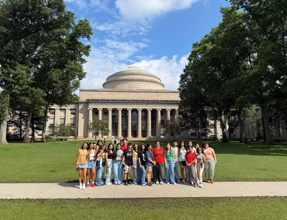 Group of people standing on a sidewalk in front of a large domed building with columns at MIT.