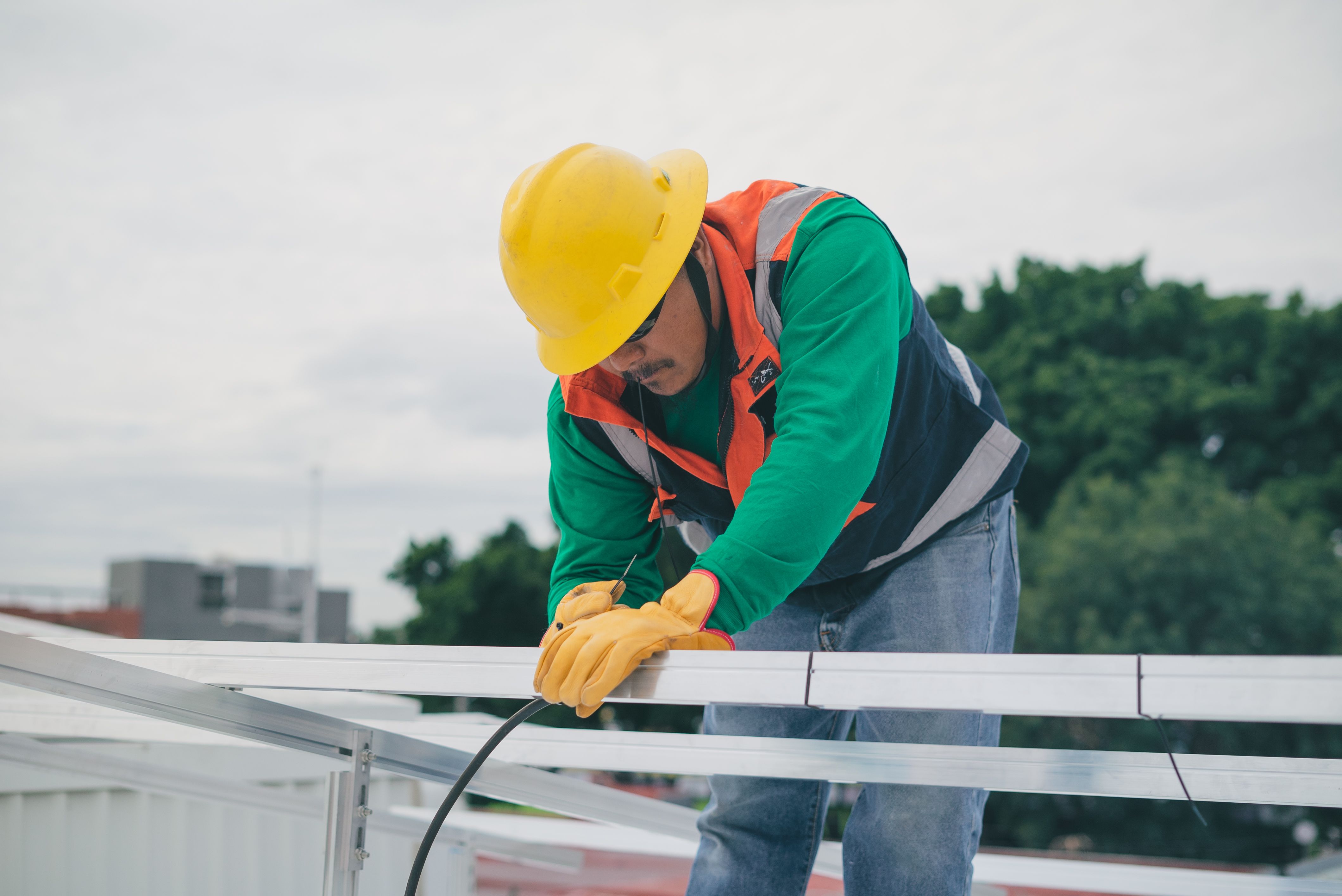 Construction worker in yellow helmet and gloves wiring metal frames outdoors.