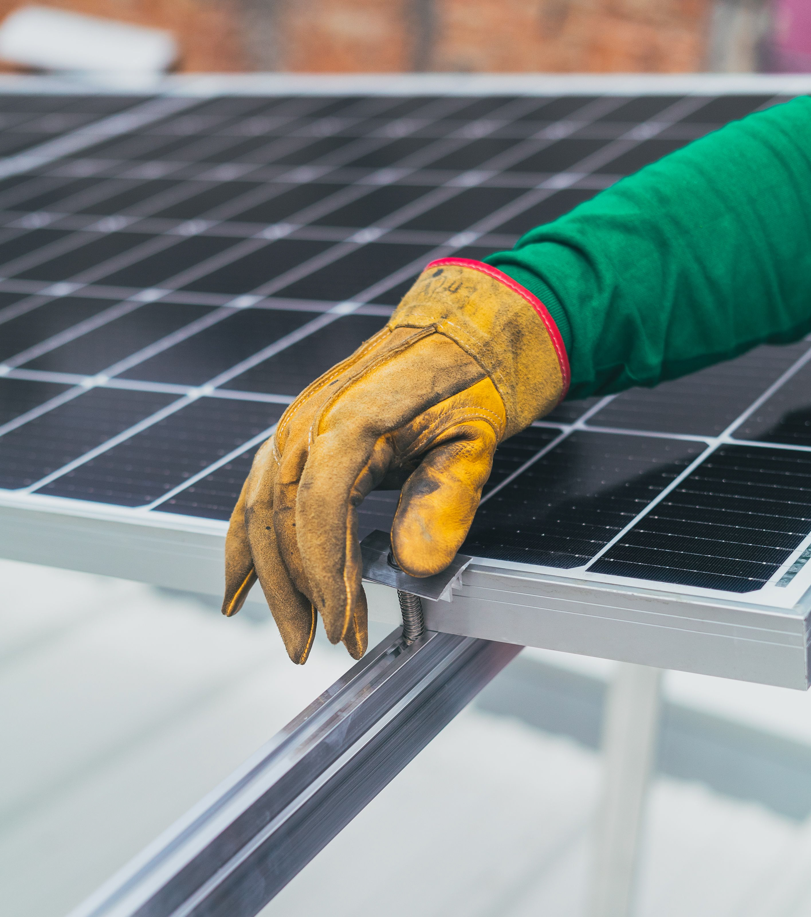 Hand in yellow work glove securing a solar panel with a bolt on metal mounting frame.