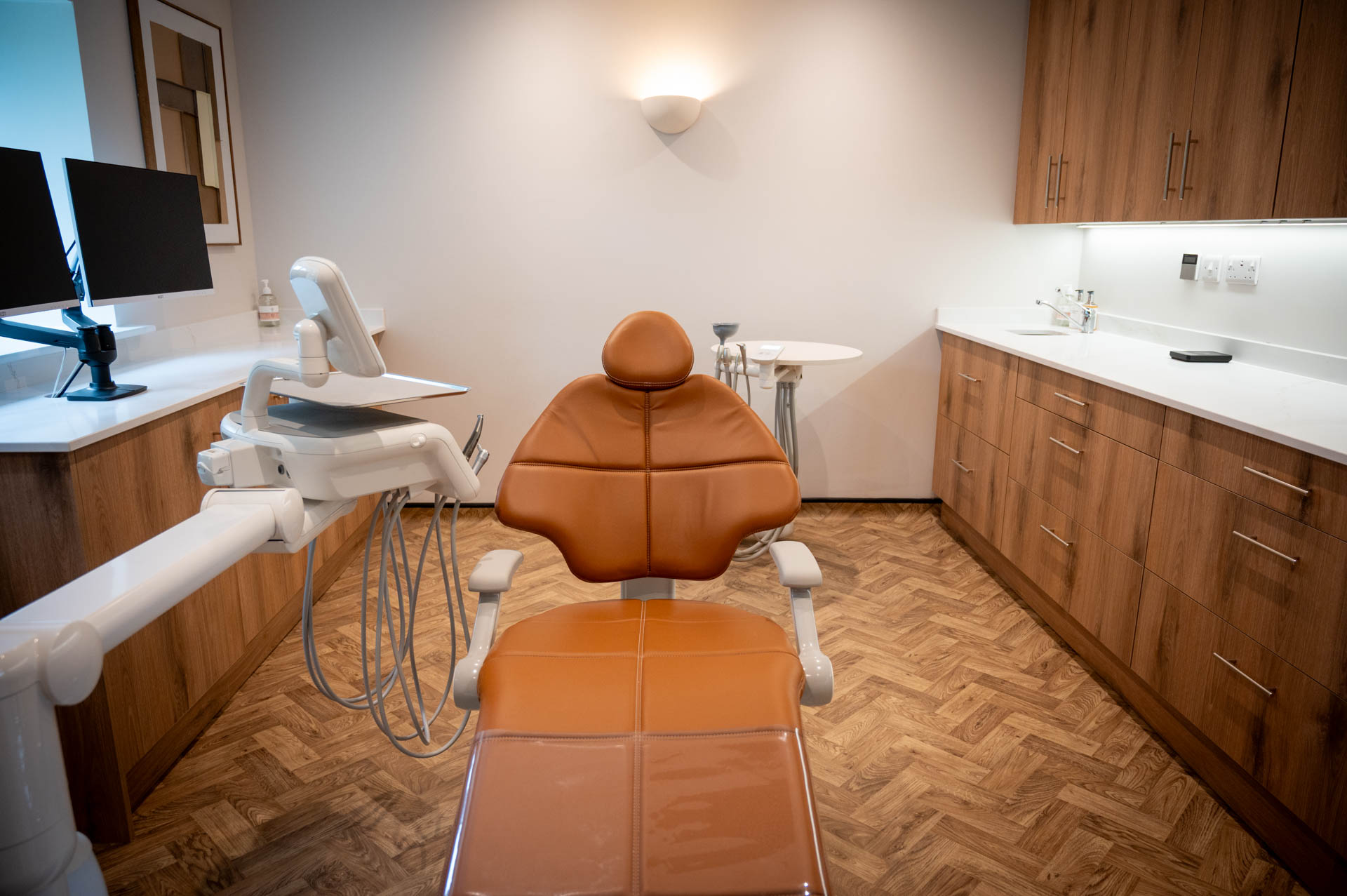 Treatment room with a tan leather dental chair and warm oak cabinetry