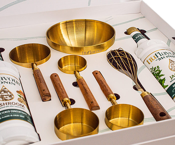 TruFlavour branded gold measuring cups, bowl, whisk, and flavor bottles in a gift box