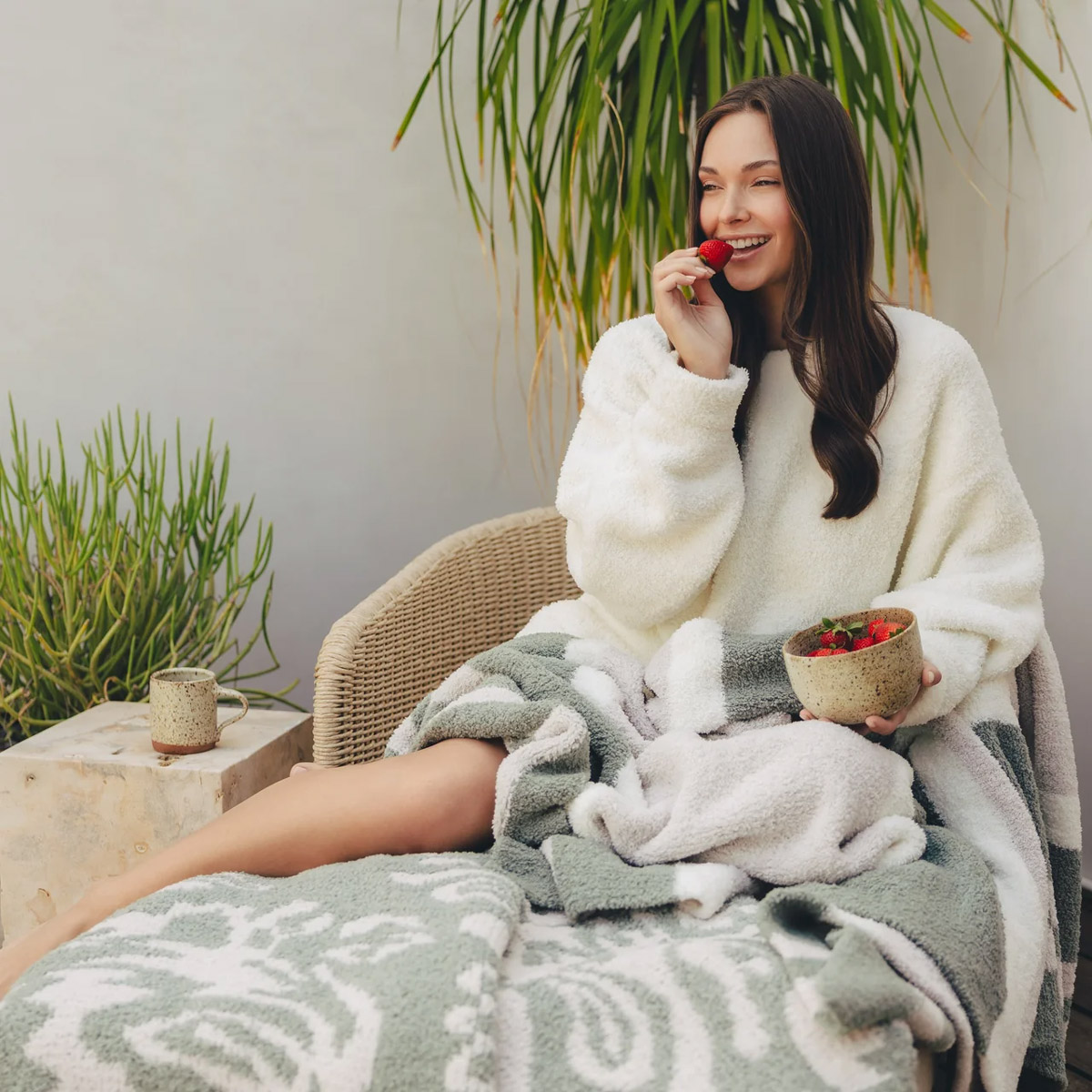 Woman relaxing outdoors with a bowl of strawberries and a branded blanket