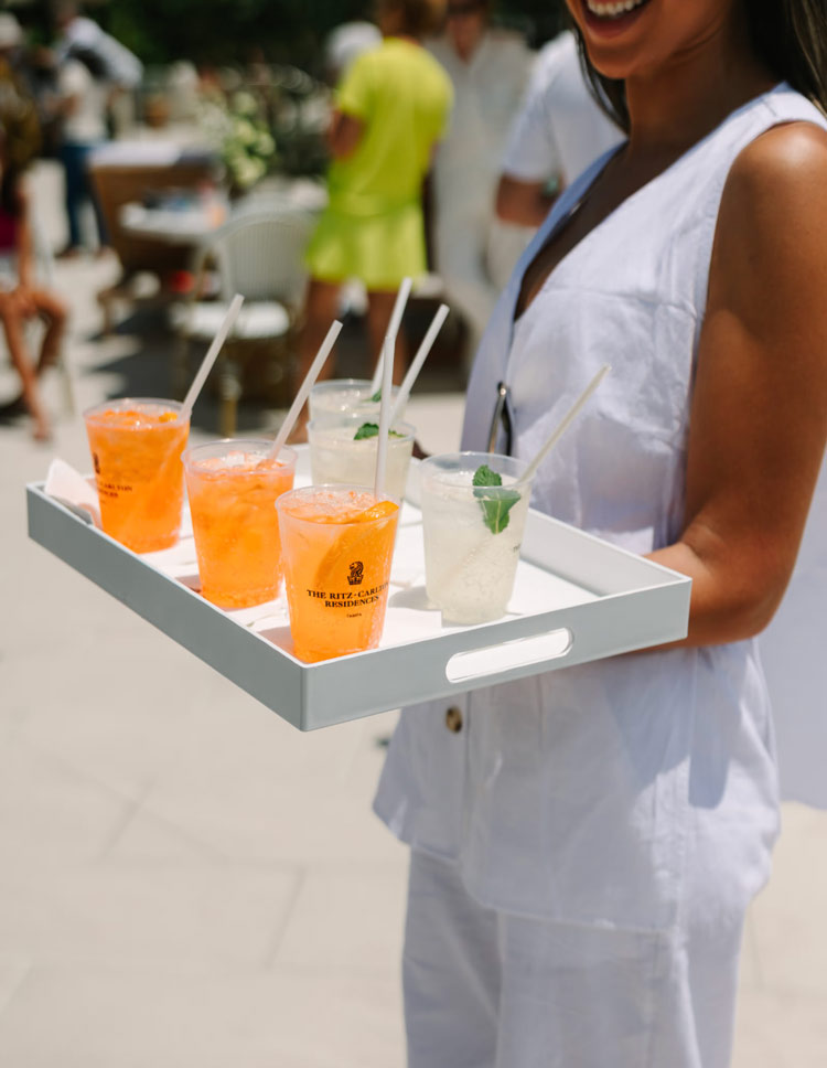 Woman serving Ritz-Carlton Residences branded drinks on a tray at an outdoor event