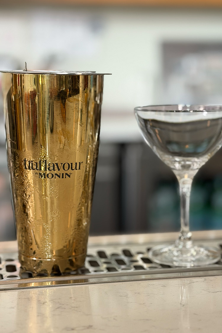 TruFlavour by Monin branded gold cocktail shaker beside a coupe glass