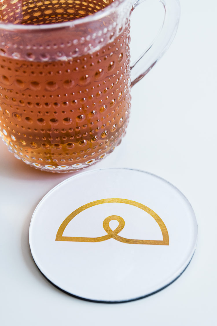 Amber drink beside a white coaster with a gold branded logo