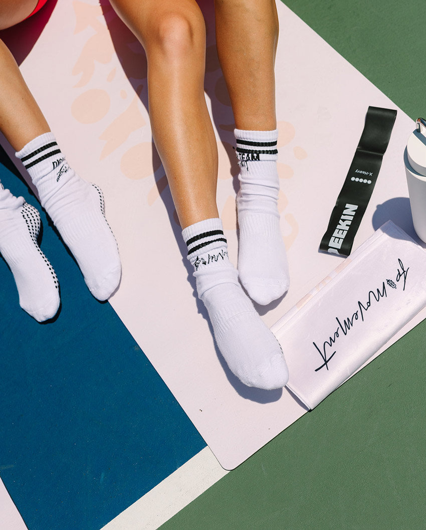 Women wearing branded athletic socks beside a resistance band and water bottle
