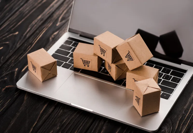 Small cardboard delivery boxes spilling out of an open laptop onto a dark wooden desk