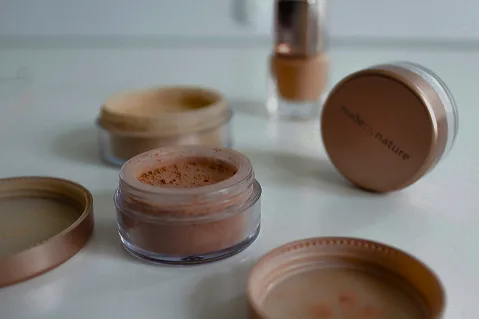 Open pots of loose powder makeup and cosmetics arranged on a pale surface