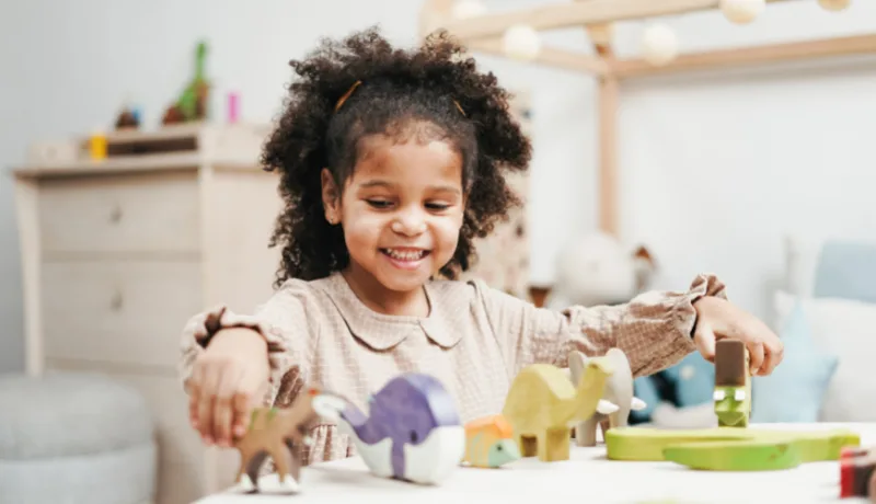 Young girl smiling as she plays with colourful toy animals at a table