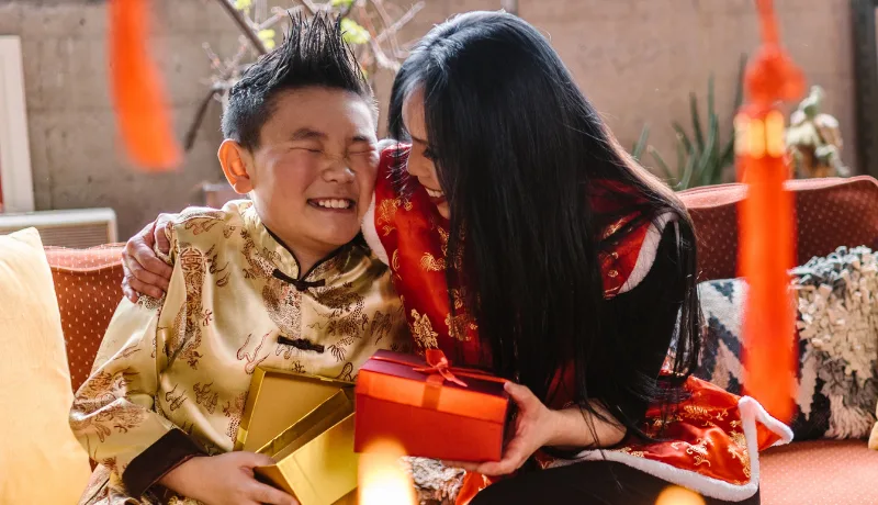 Two children in traditional dress laughing together with red and gold gifts during Chinese New Year