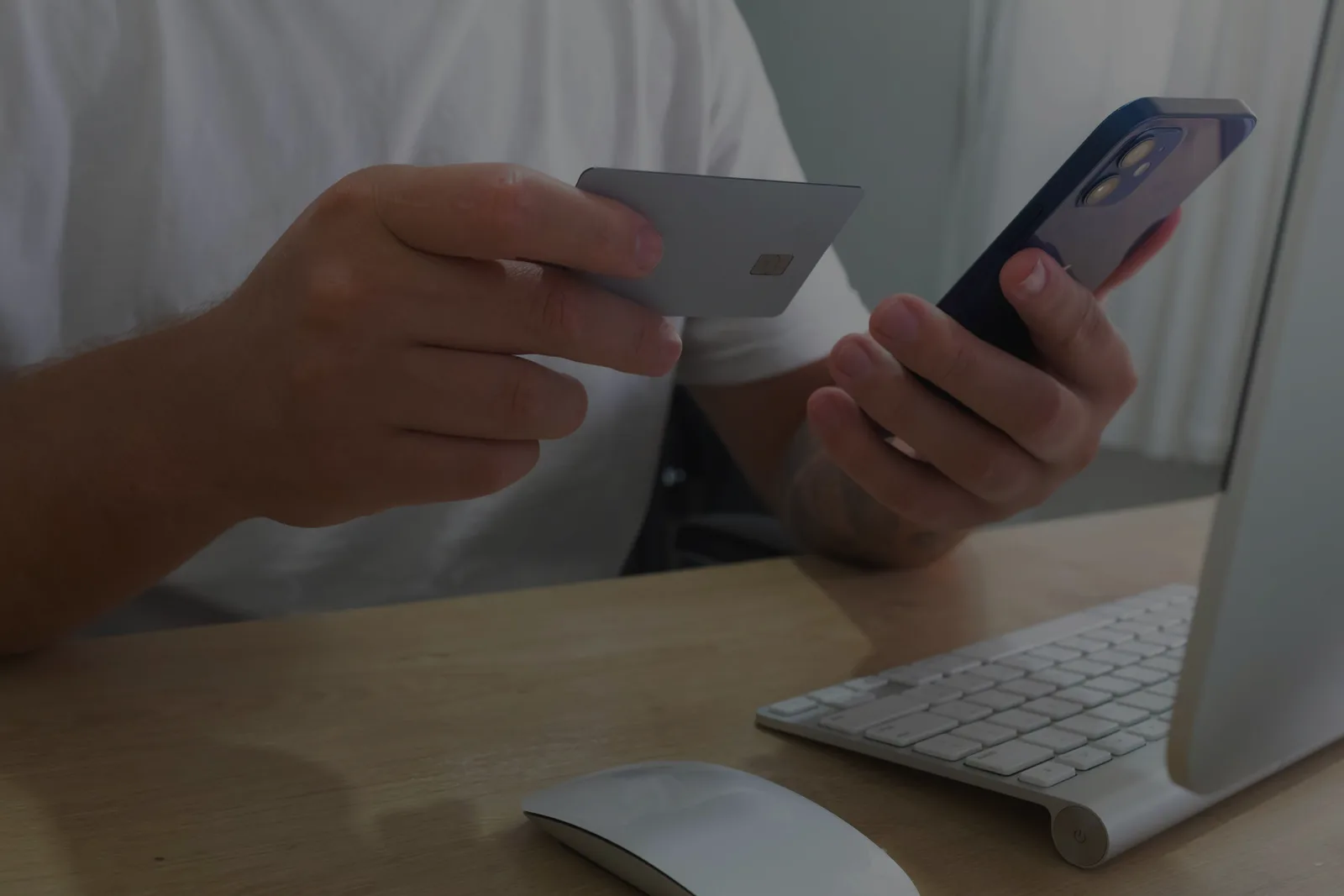Person holding a smartphone while working at a desktop computer