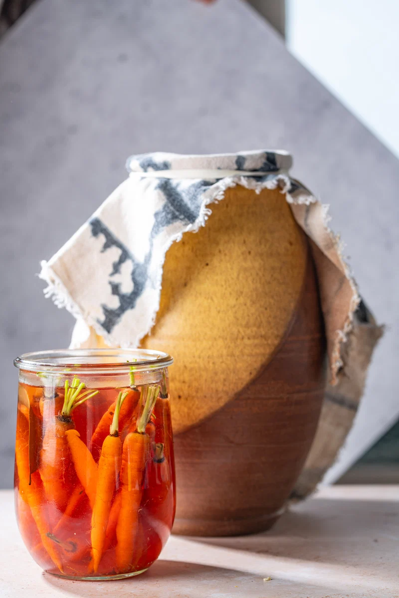 Jar of pickled carrots beside a ceramic crock