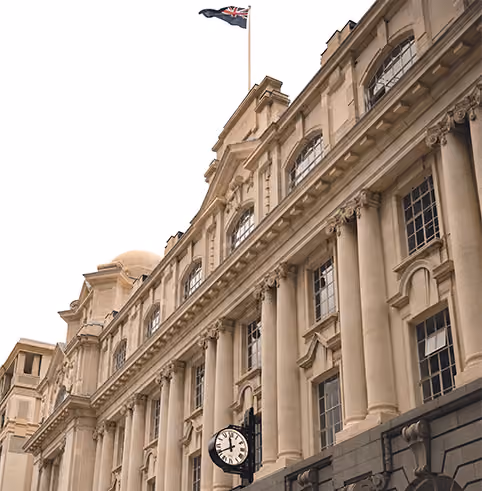 Historic building facade with tall classical columns and large windows, a clock showing 1:07, and a flag featuring the Union Jack flying at the top.