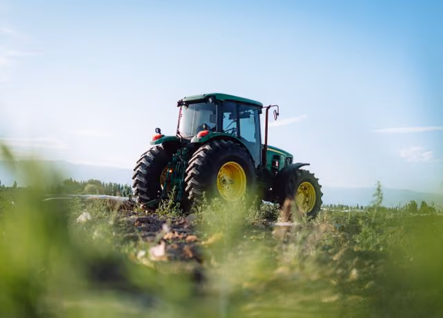 Green tractor with large yellow wheels parked on a rural field under a clear blue sky.