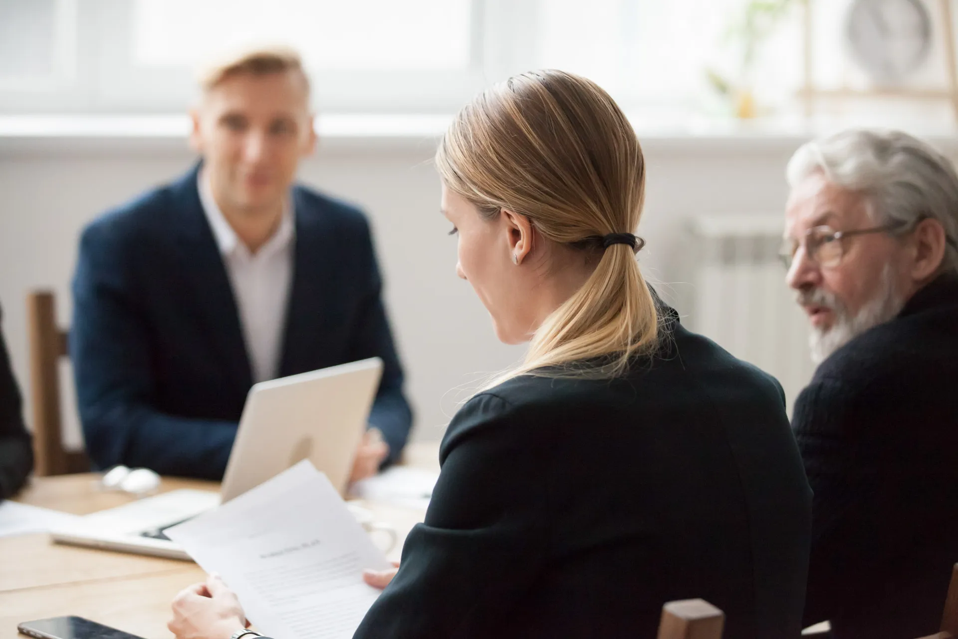 Businesswoman reading a document during a meeting with two colleagues in a bright office.