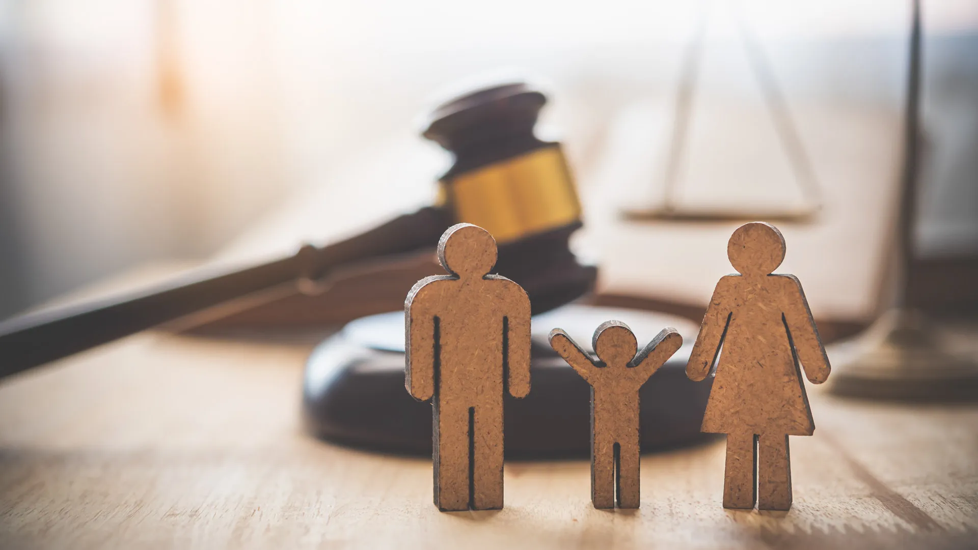 Wooden figures of a man, child, and woman in front of a judge’s gavel and scales of justice.