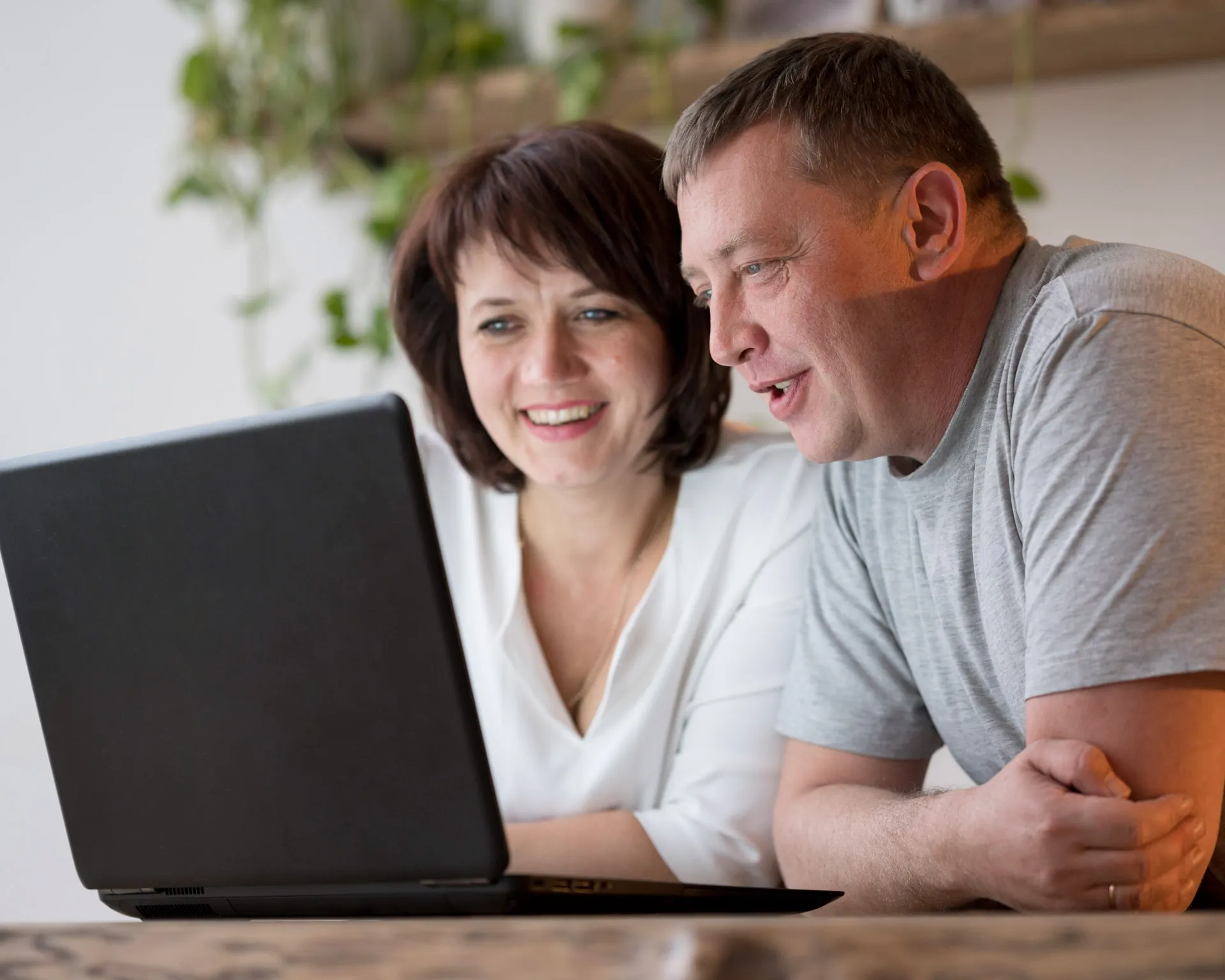 Smiling middle-aged couple looking at a laptop screen together at home.