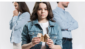 Young girl holding a wooden model house with two adults facing away in the background.