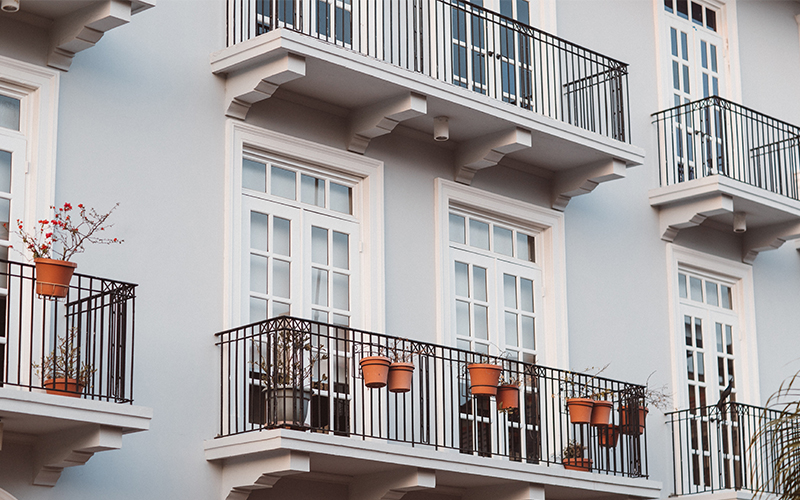 Building facade with white framed windows and balconies holding potted plants.