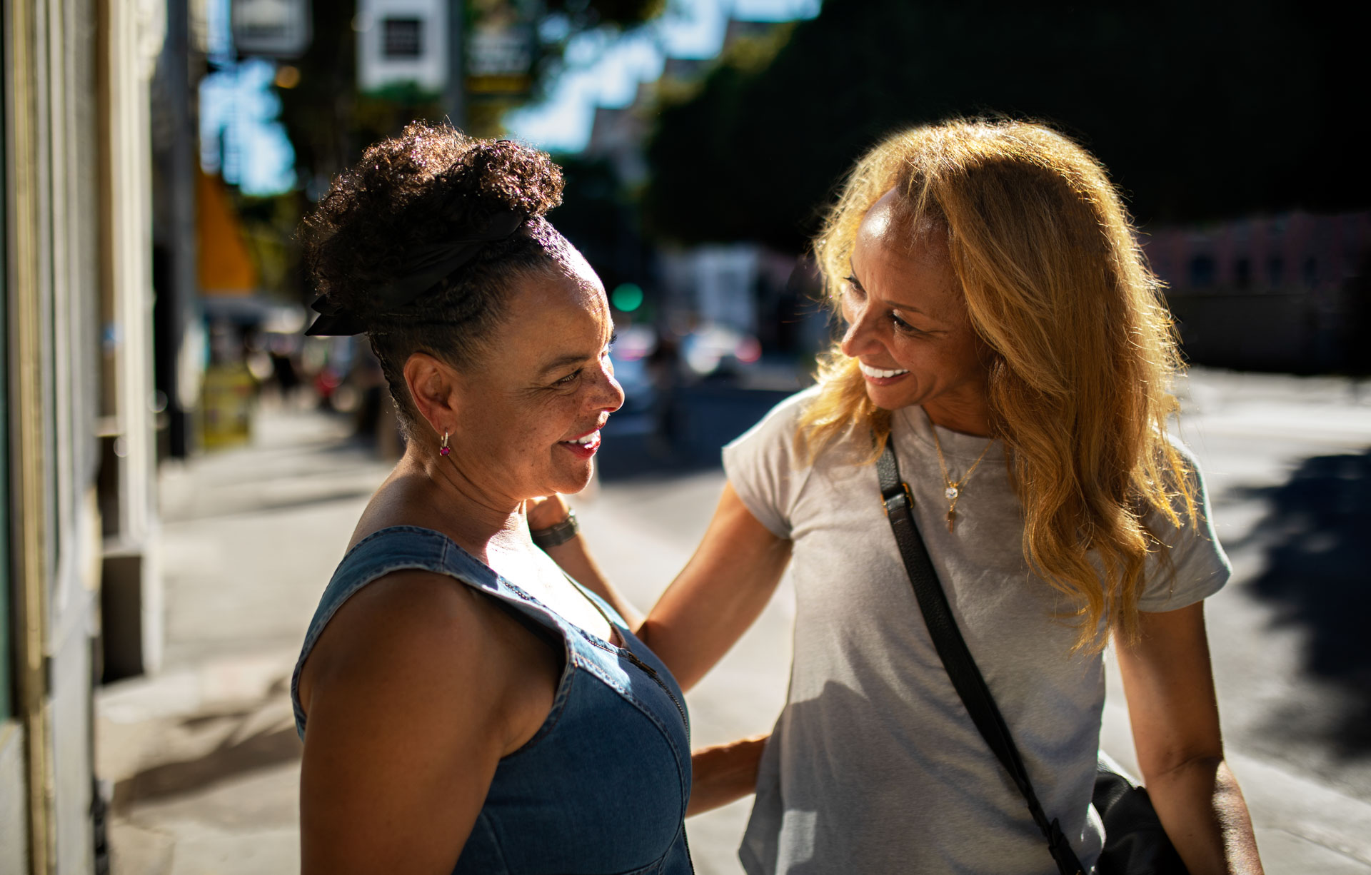 Two happy senior women smiling and talking together while walking on a sunny city sidewalk.