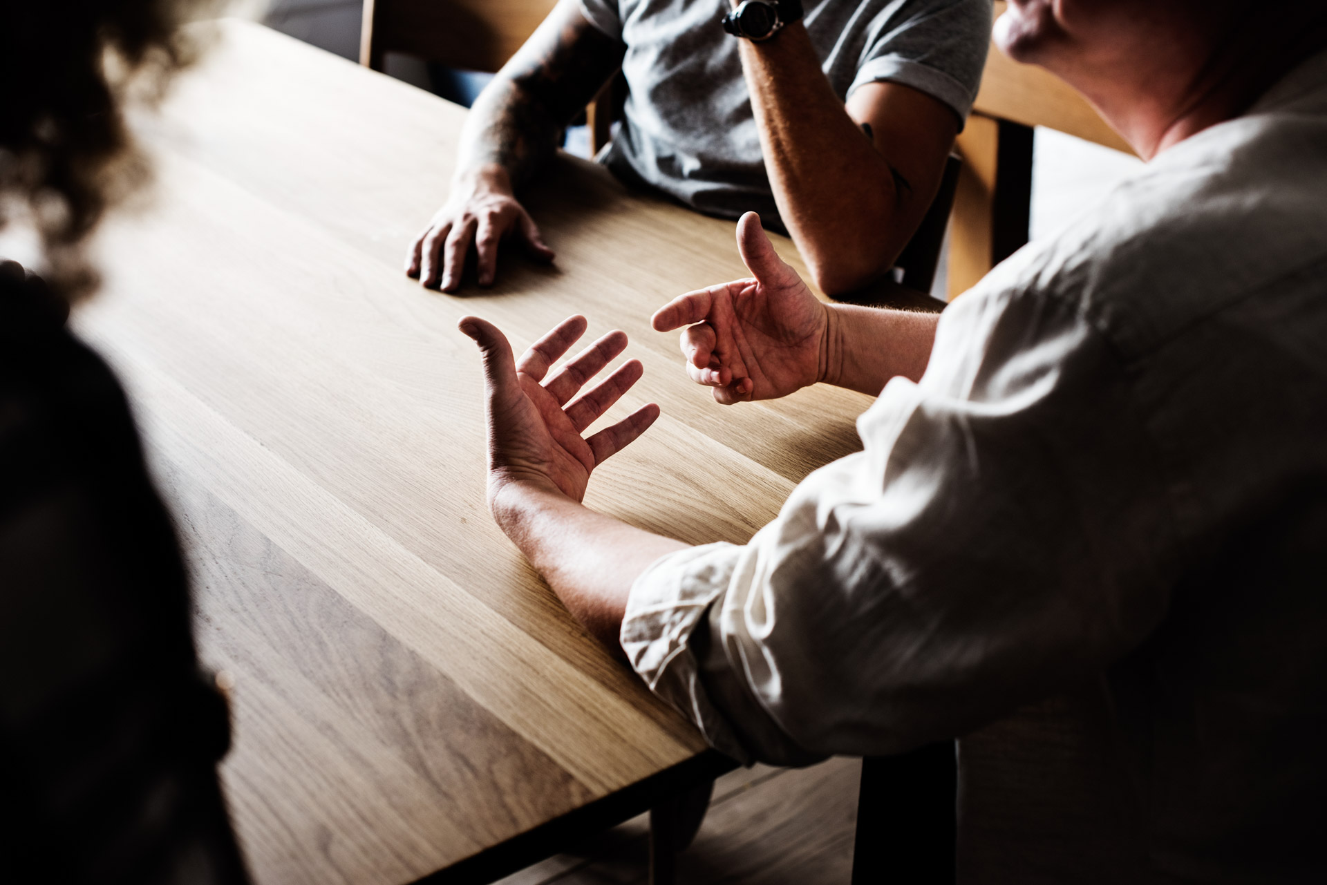 Hands of three people engaged in a discussion over a wooden table.