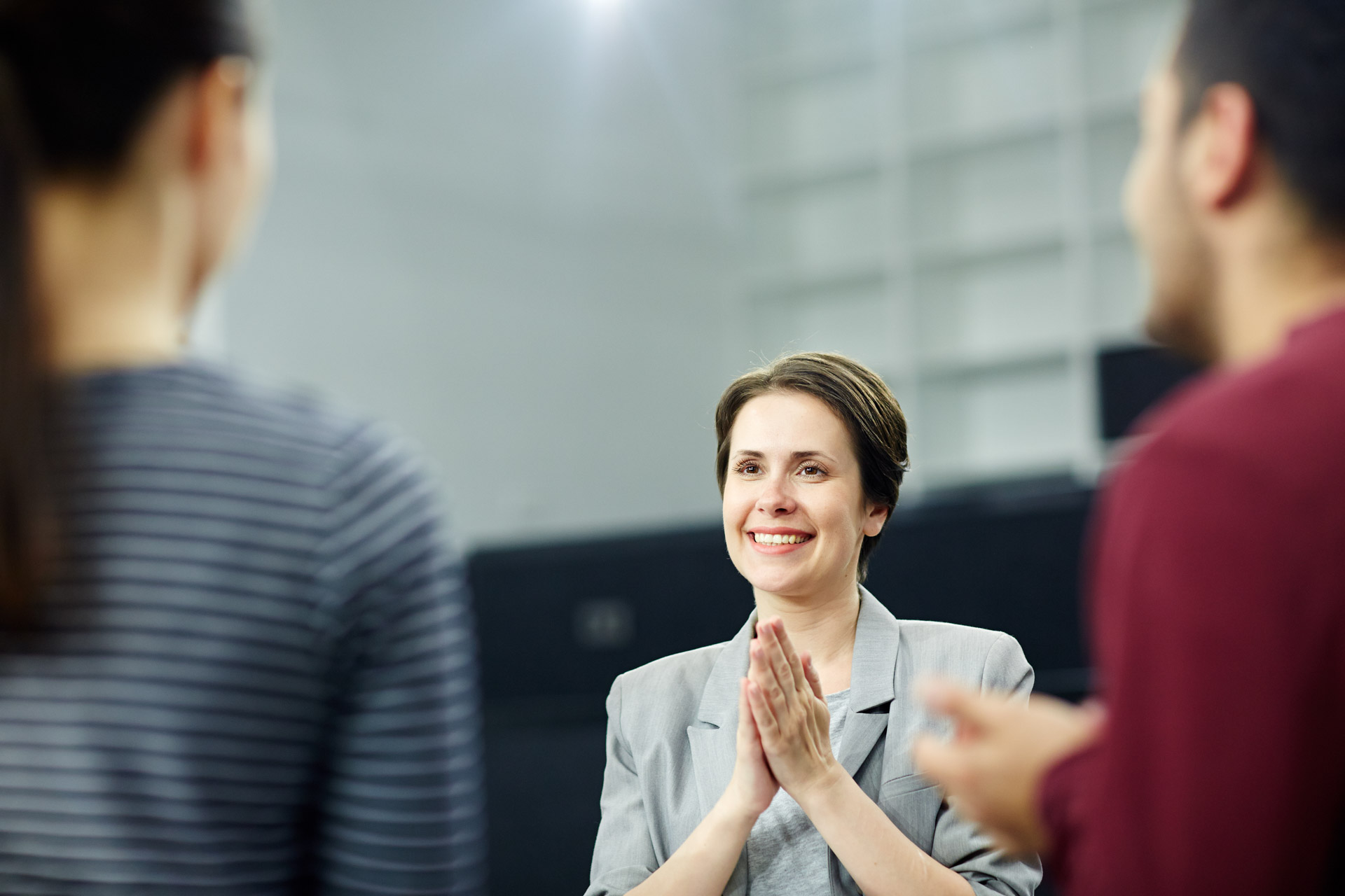 Smiling woman clapping hands facing two people in a casual indoor setting.