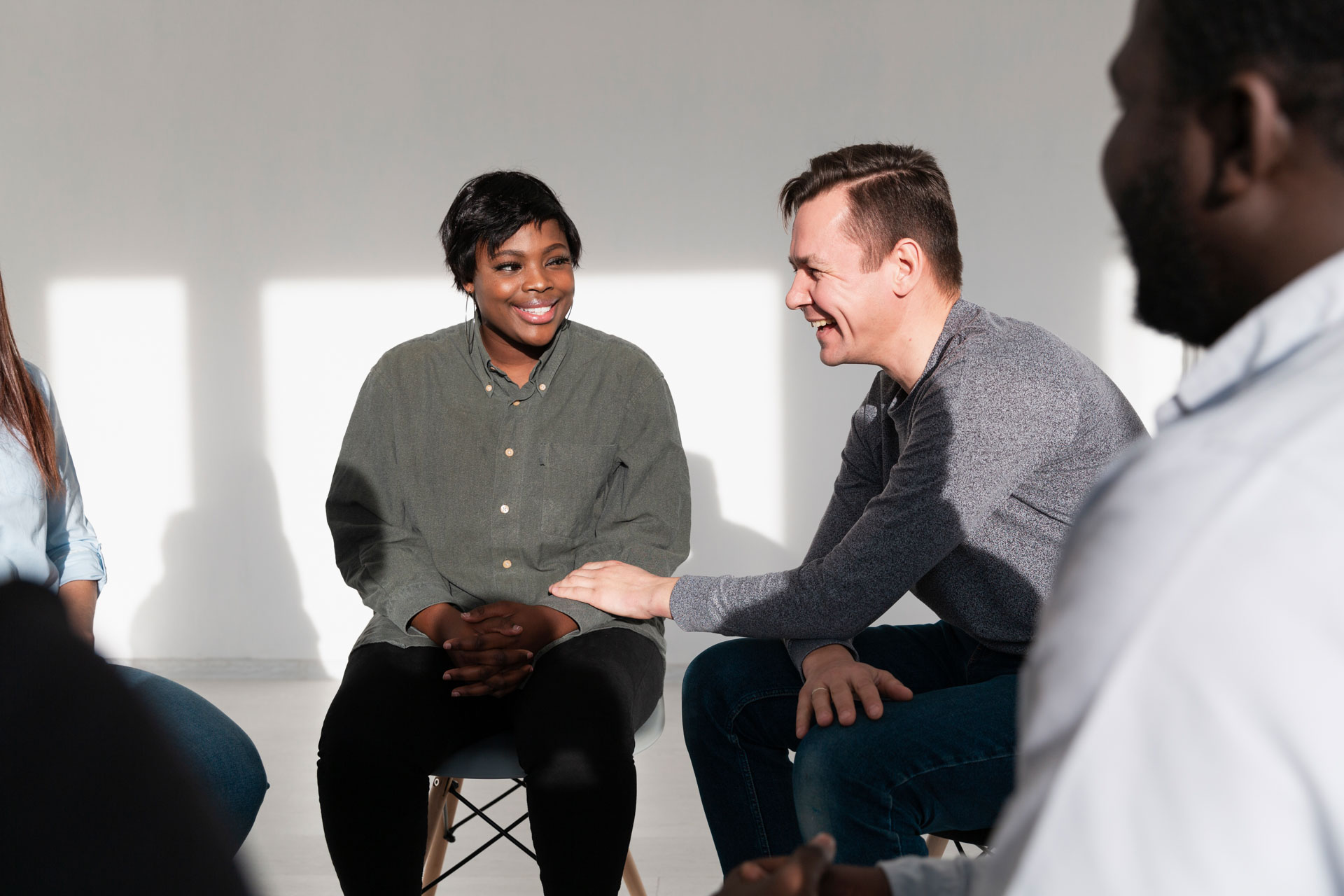 Man encouraging smiling woman sitting in a circle with others during a group discussion.