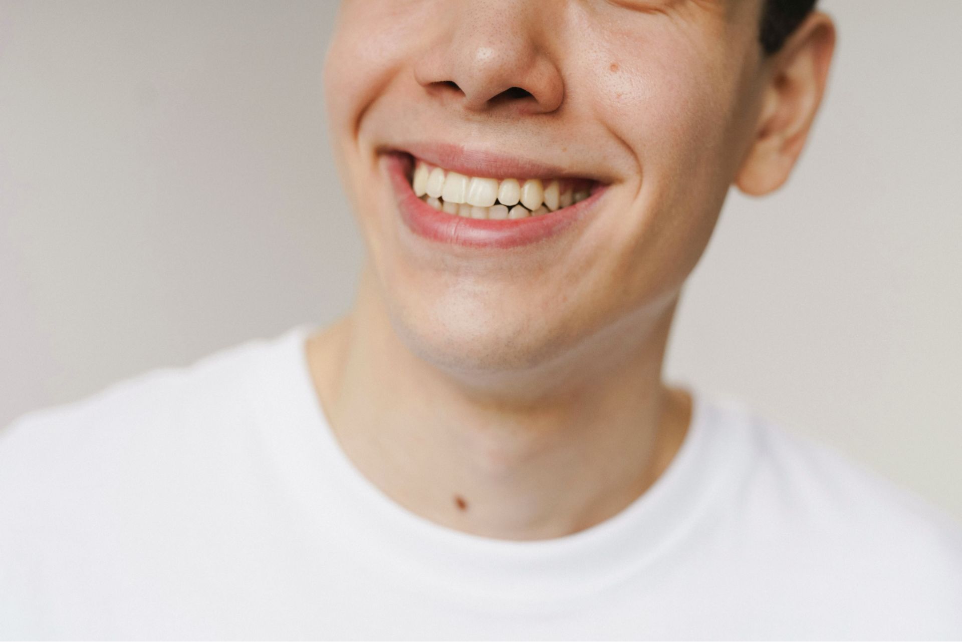Close-up of a smiling young man's lower face showing teeth and part of his white shirt.