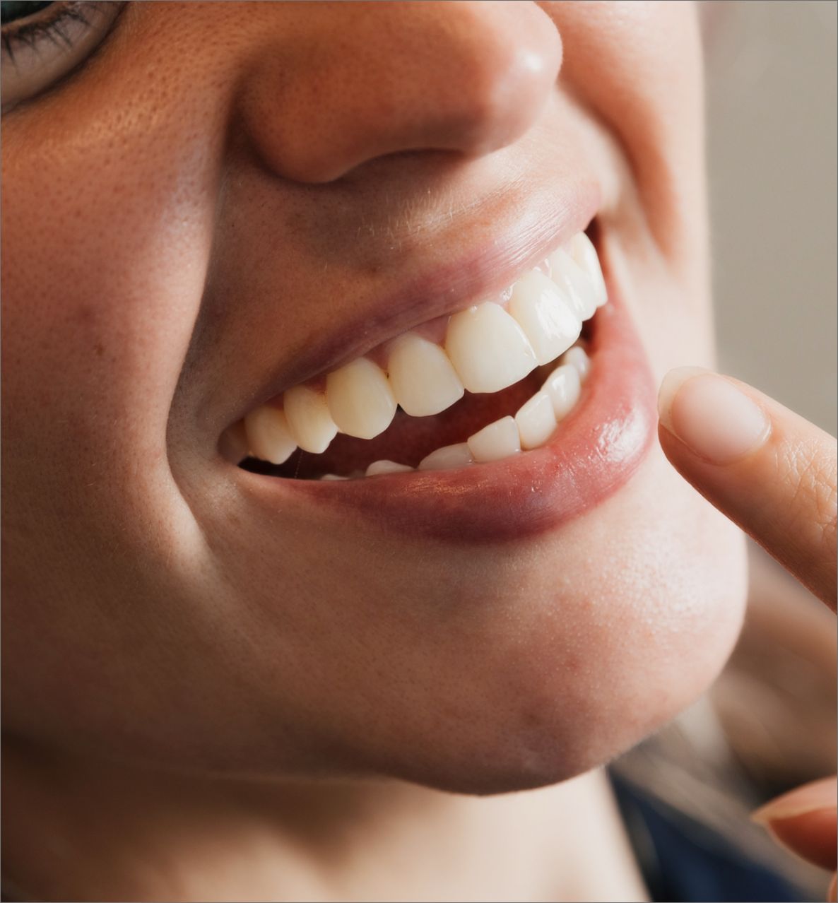 Close-up of a person smiling, showing white teeth with a finger near the lower lip.