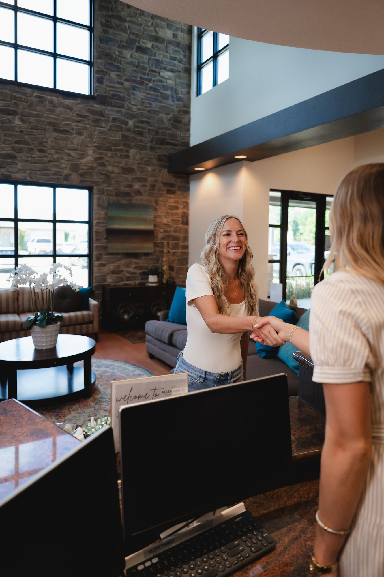 Smiling woman shaking hands with receptionist at a modern dental office reception.