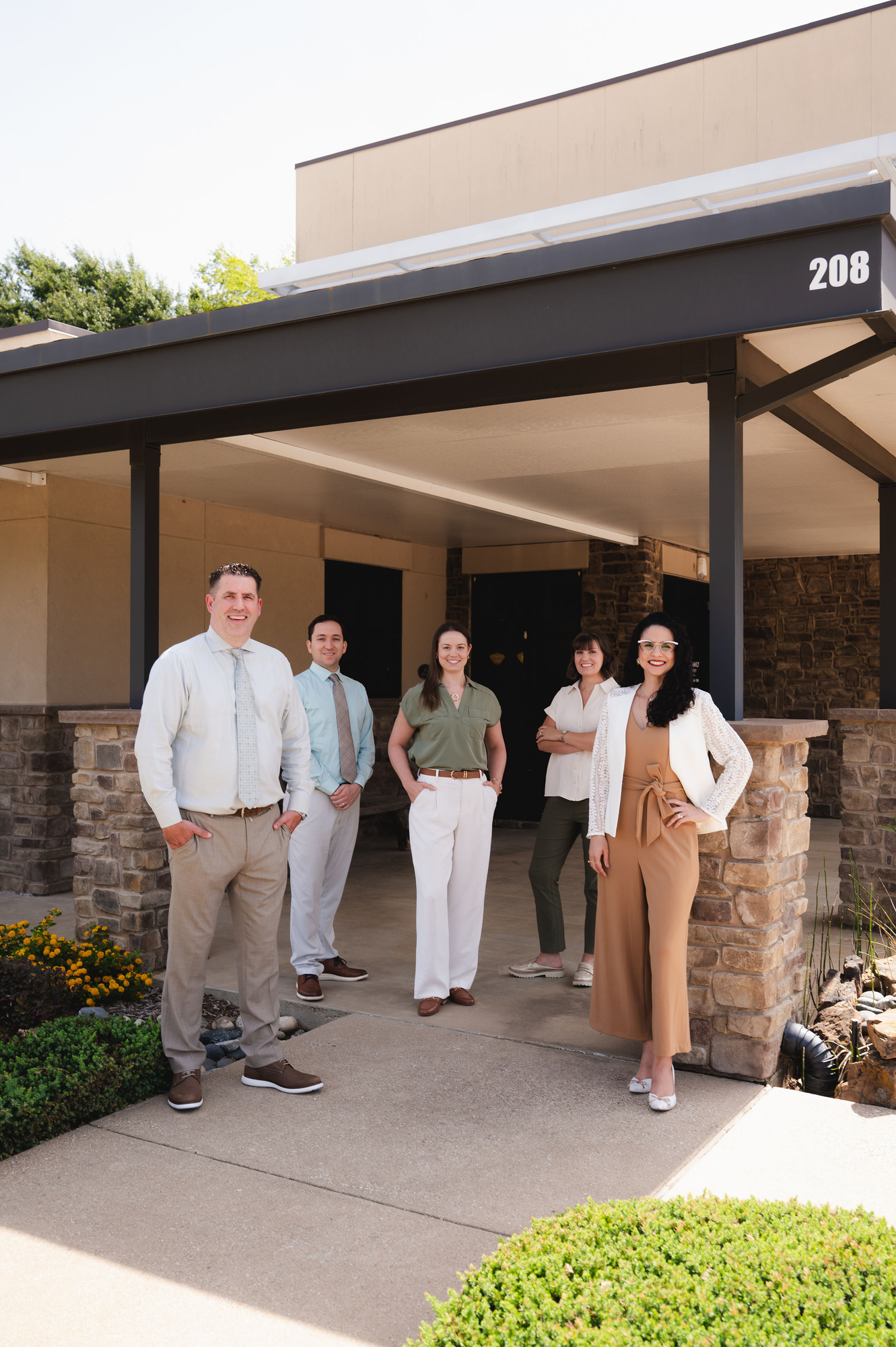 Five professionally dressed people standing outside a building entrance marked with number 208.
