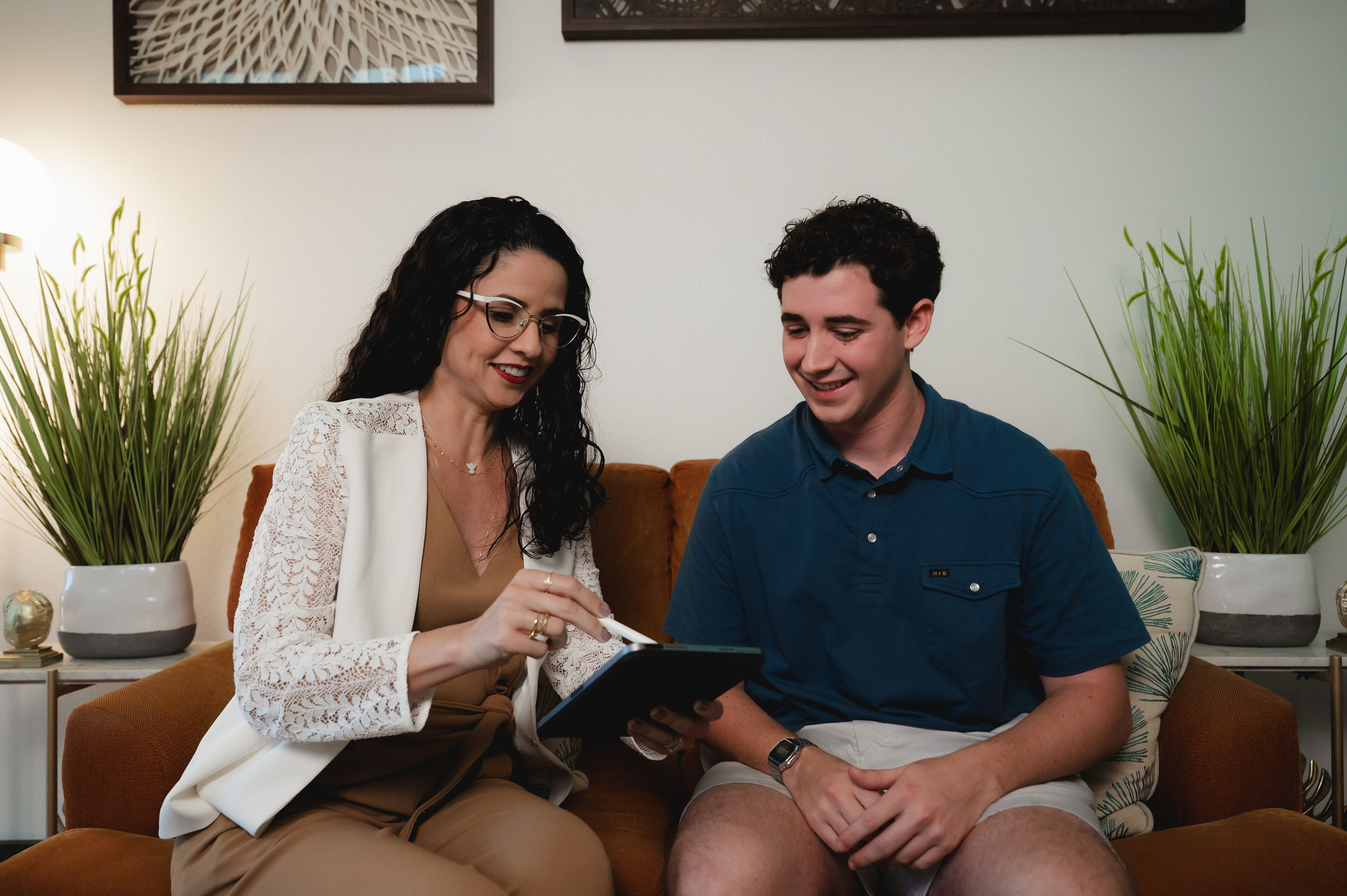 Woman with glasses showing a tablet to a smiling man sitting beside her on a brown couch.