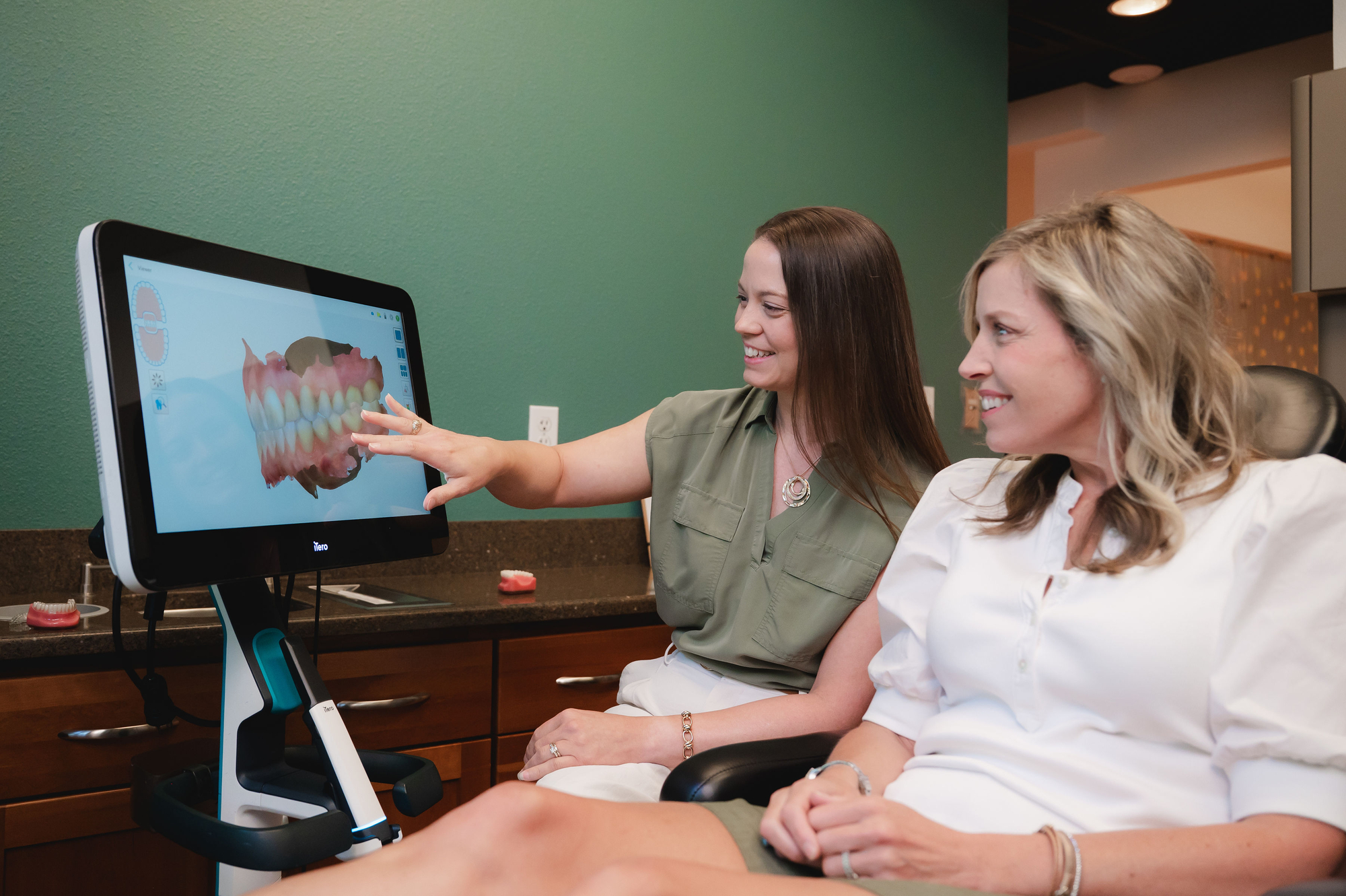 Dentist showing a digital 3D dental scan on a screen to a smiling patient in a dental office.