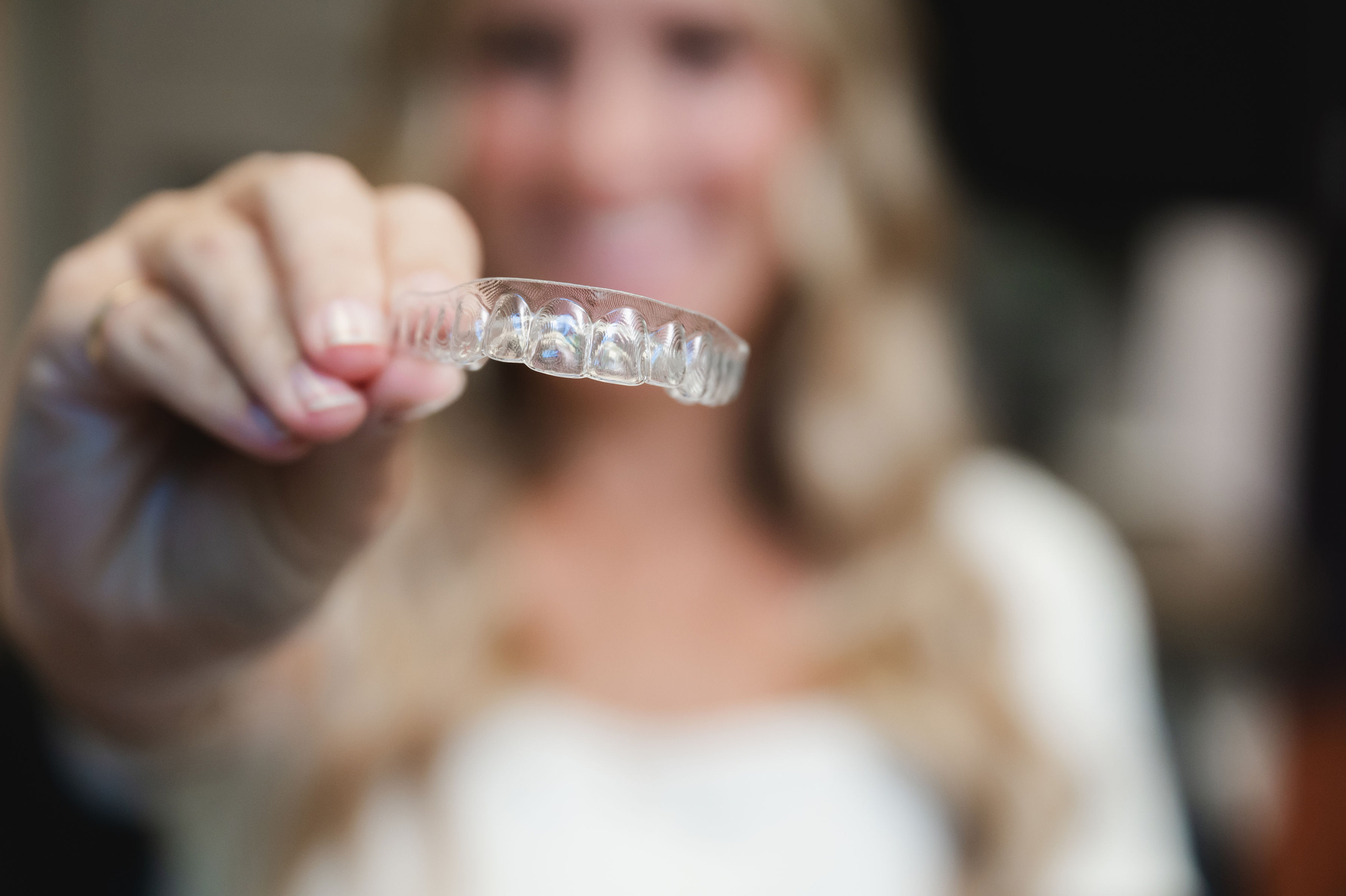 Woman holding a transparent orthodontic aligner in front of her smiling face.