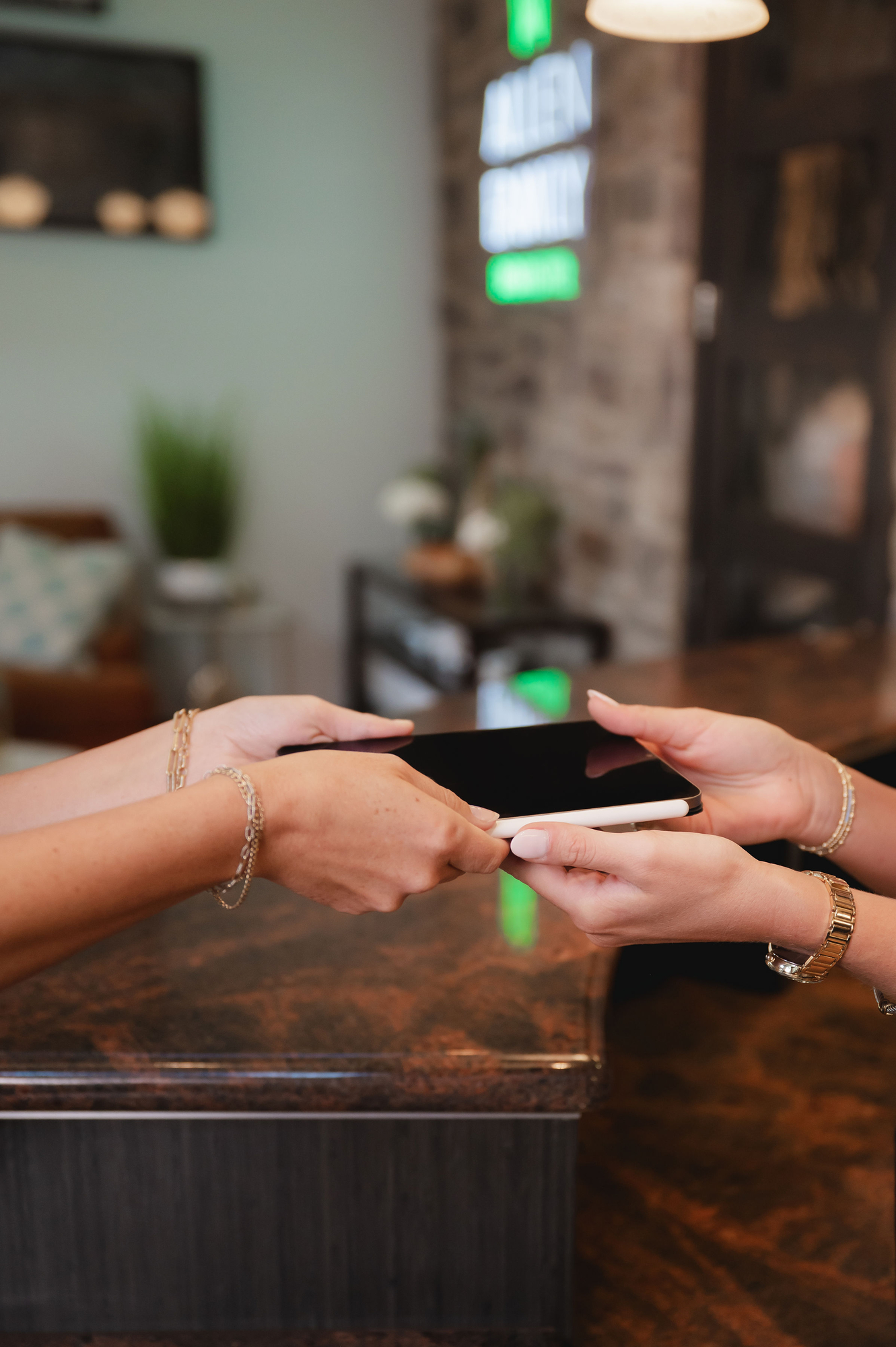 Two people exchanging a tablet with a stylus over a brown countertop in a cozy office.