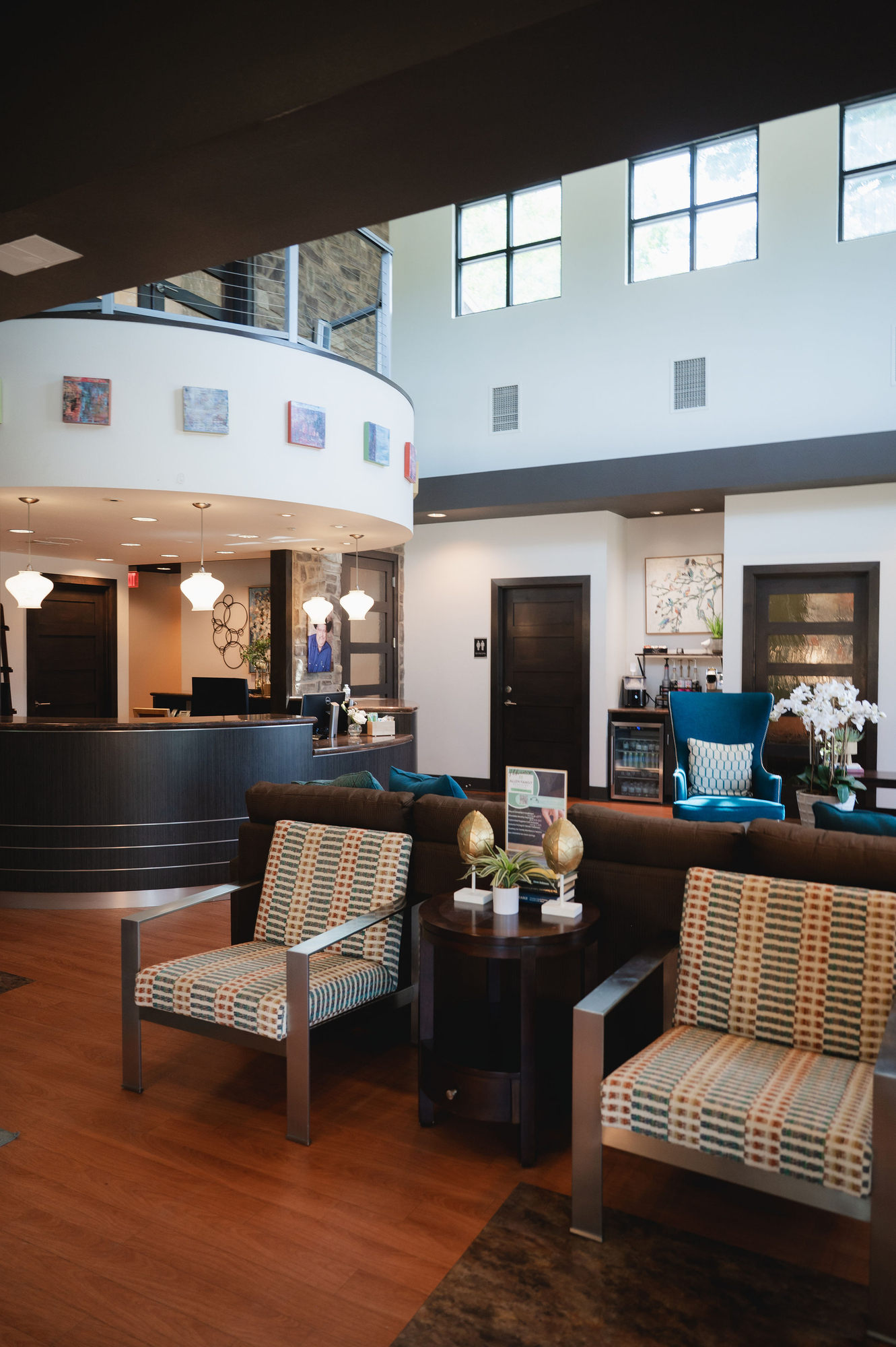 Modern dental office waiting area with patterned chairs, brown couch, and curved reception desk.