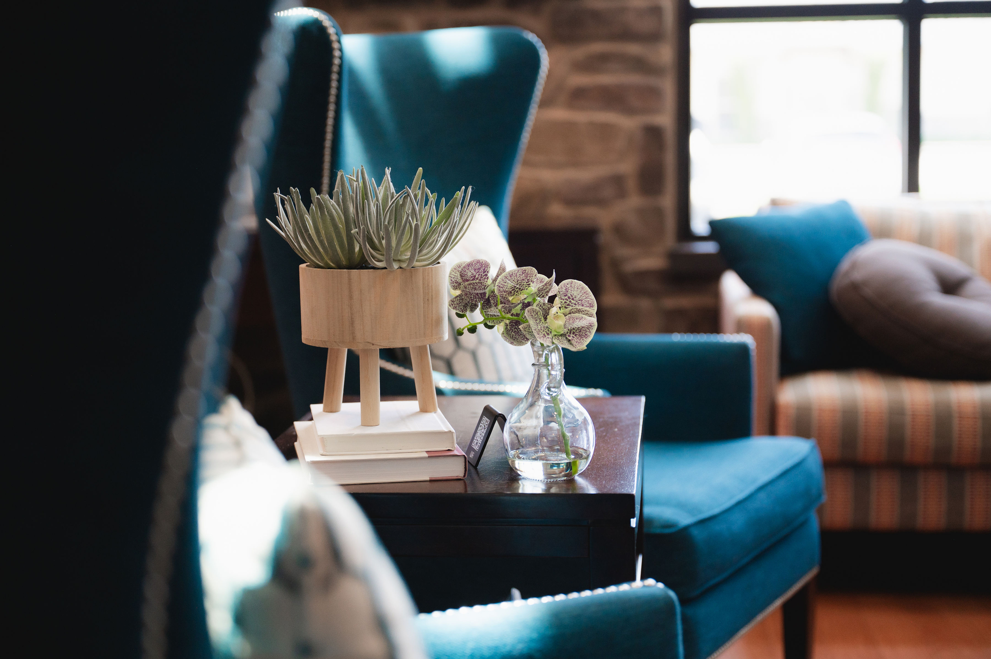 Living room with blue armchairs, a side table holding a wooden planter, books, and a glass vase with flowers.
