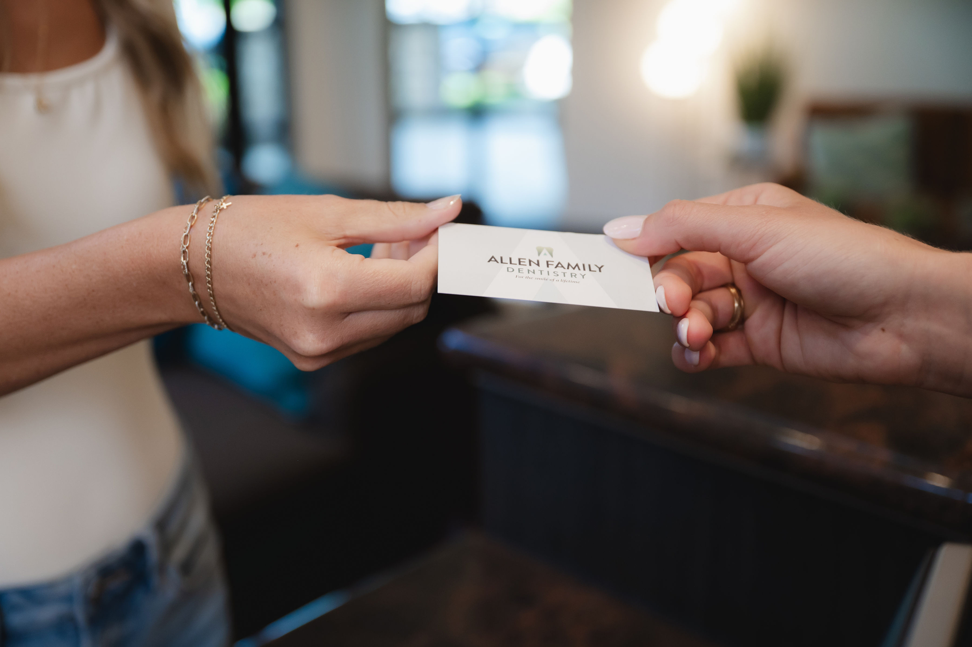Two people exchanging a business card that reads Allen Family Dentistry in an office setting.