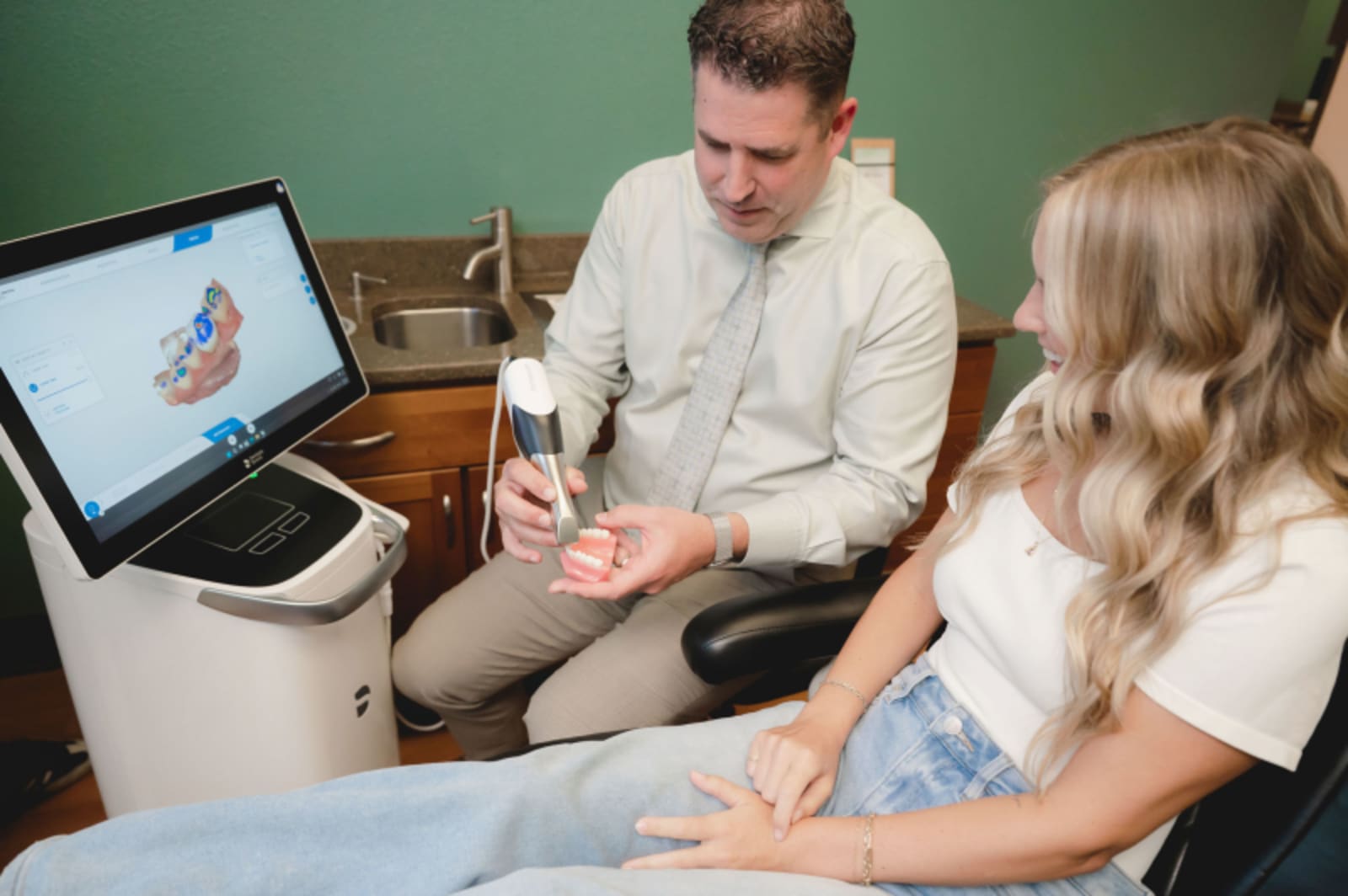 Dentist discussing treatment plan with female patient while reviewing digital scan on computer monitor.