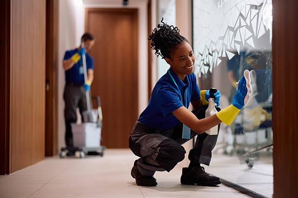 Cleaner disinfecting a glass partition while another cleaner works in the background.