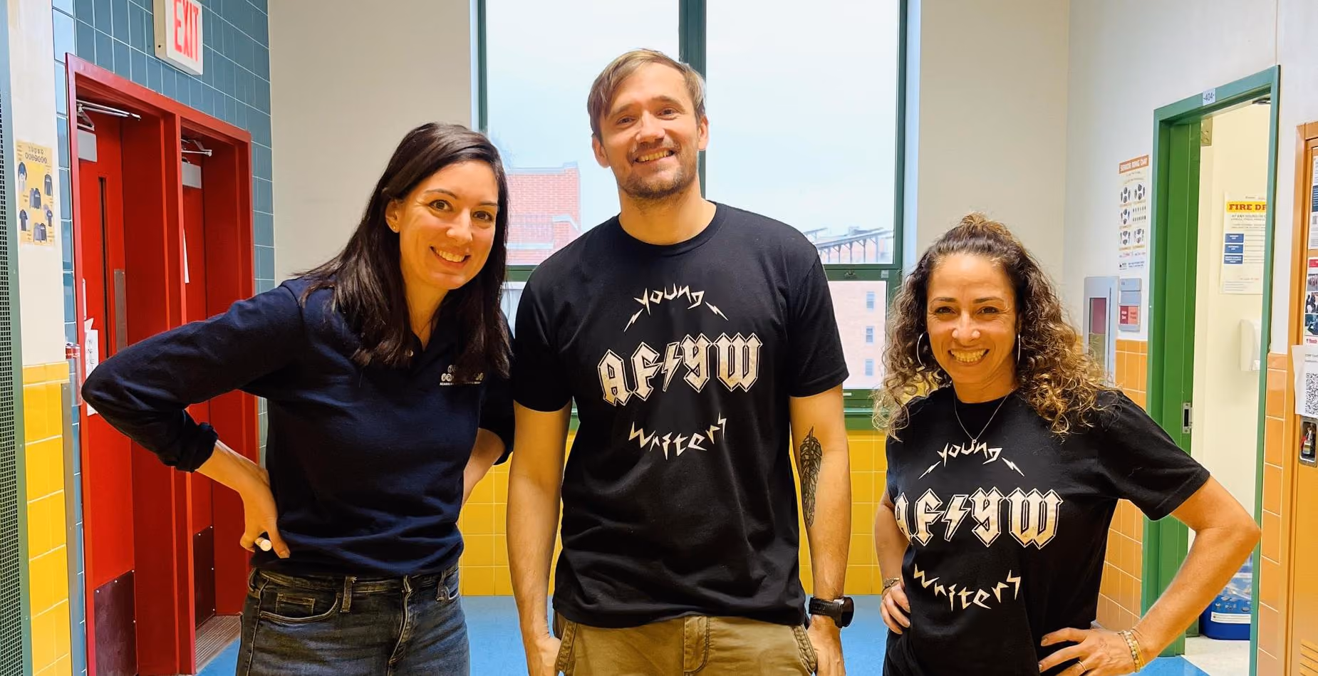 Three smiling staff members posing together in a school hallway