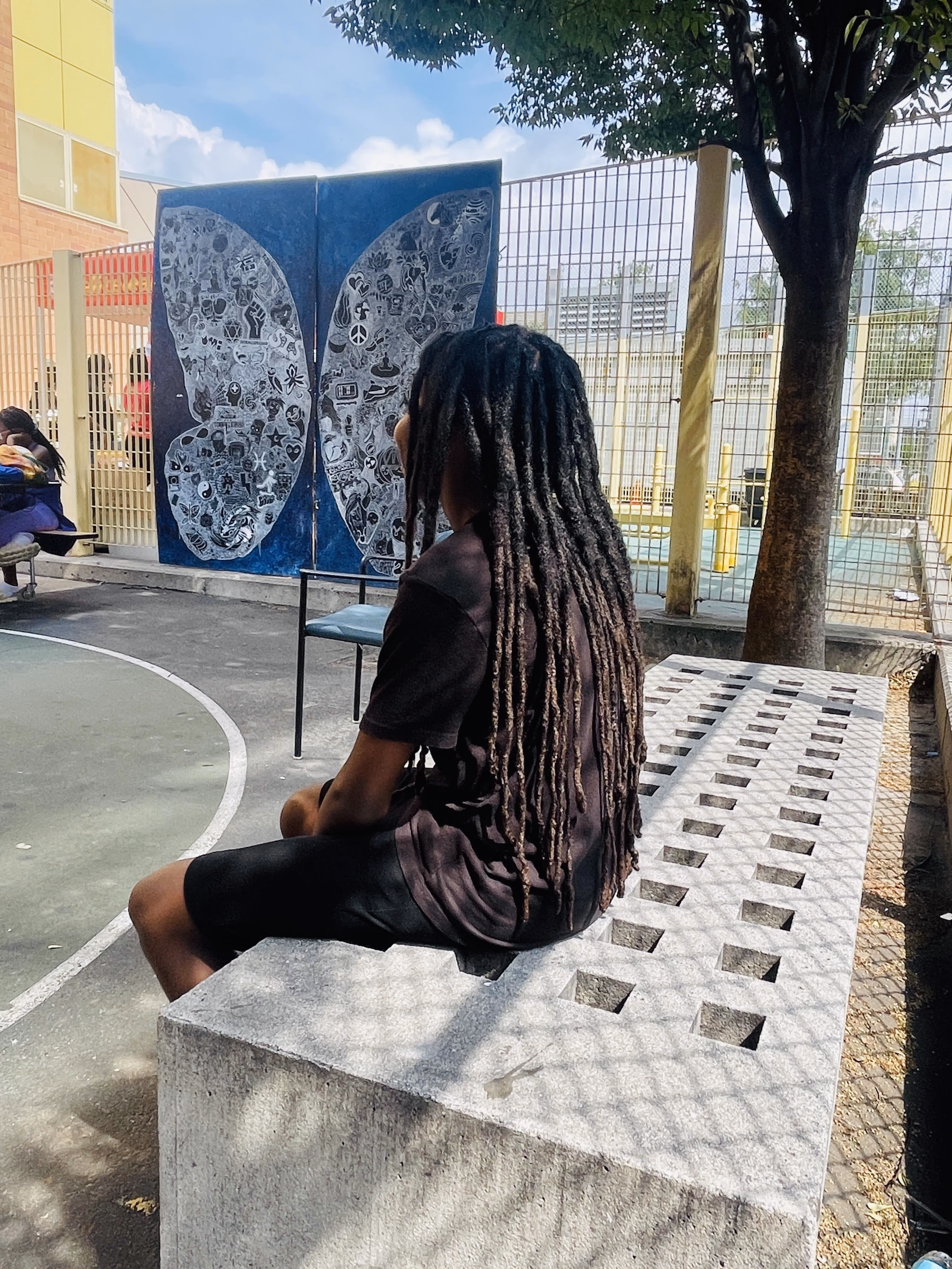 Student with locs sitting outdoors viewing a butterfly mural artwork