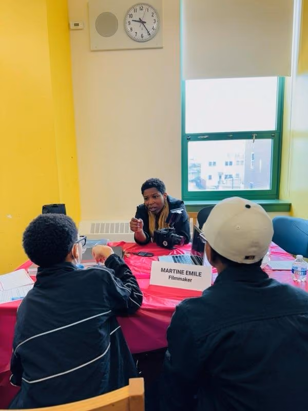 Filmmaker Martine Emile speaks with two students at a table
