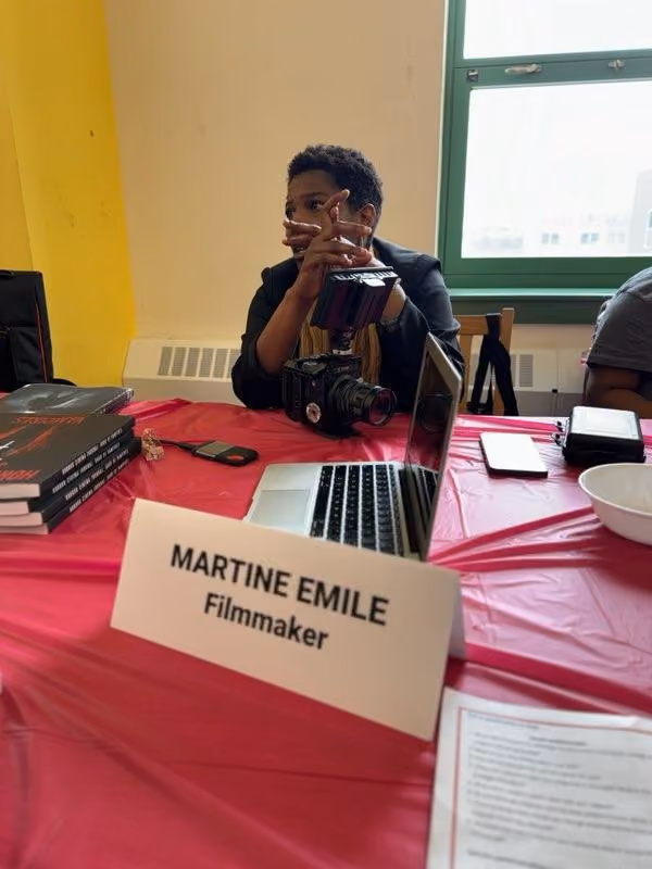 Filmmaker Martine Emile seated at table with camera and laptop