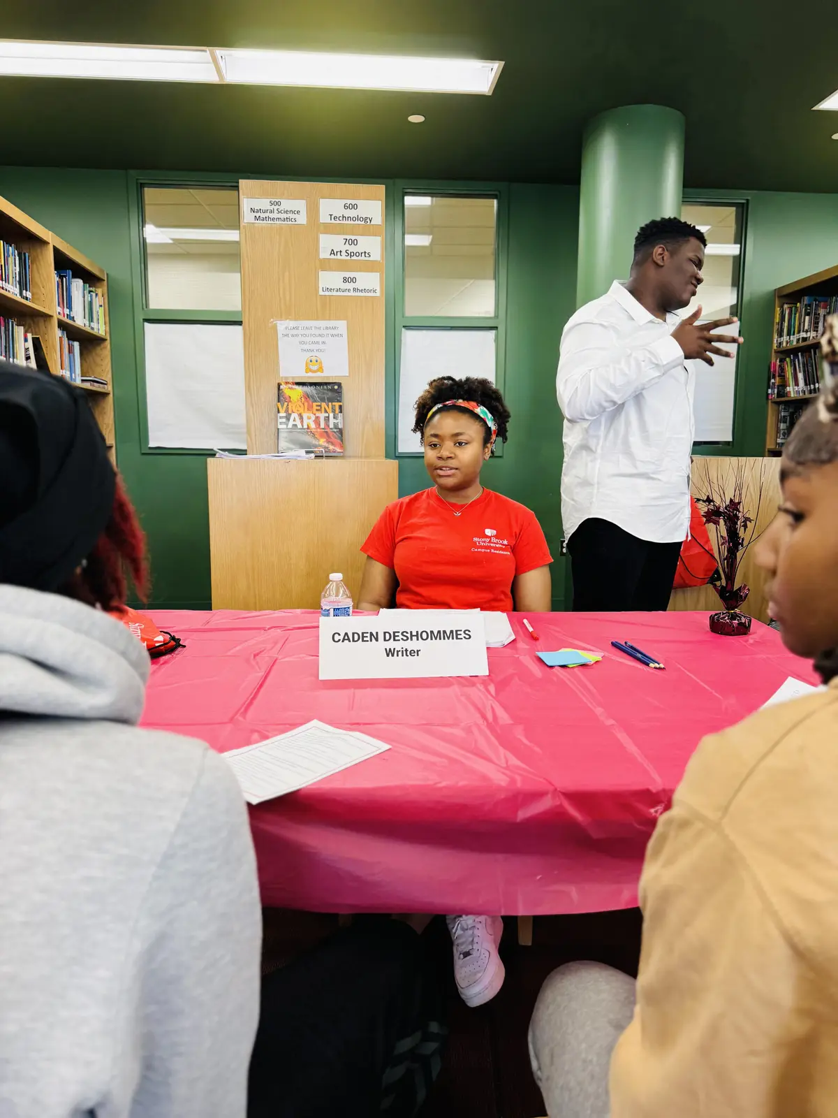 Student writer Caden Deshommes seated at table during school library event