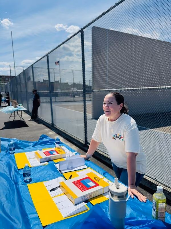 Volunteer smiling at outdoor registration table with folders and forms