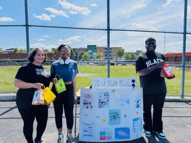 Three students presenting a Mental Health Matters project board outdoors